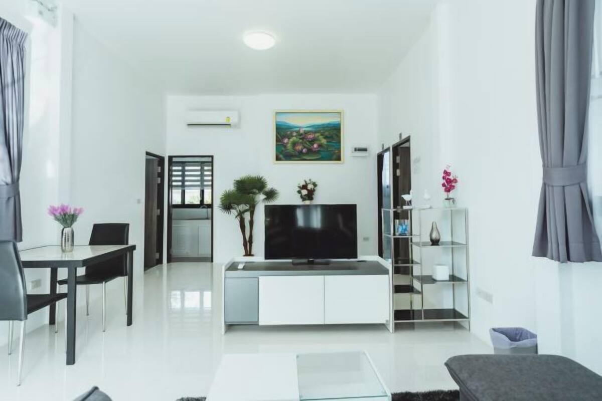 Un soggiorno moderno con una TV a schermo piatto, un'area pranzo con tavolo e sedie, un tavolino da caffè in vetro e un divano.