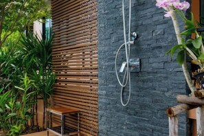 Una ducha con manguera, una pared de listones de madera y una planta.