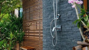 Une douche avec un mur en pierre, un mur en bois à lattes et une plante.
