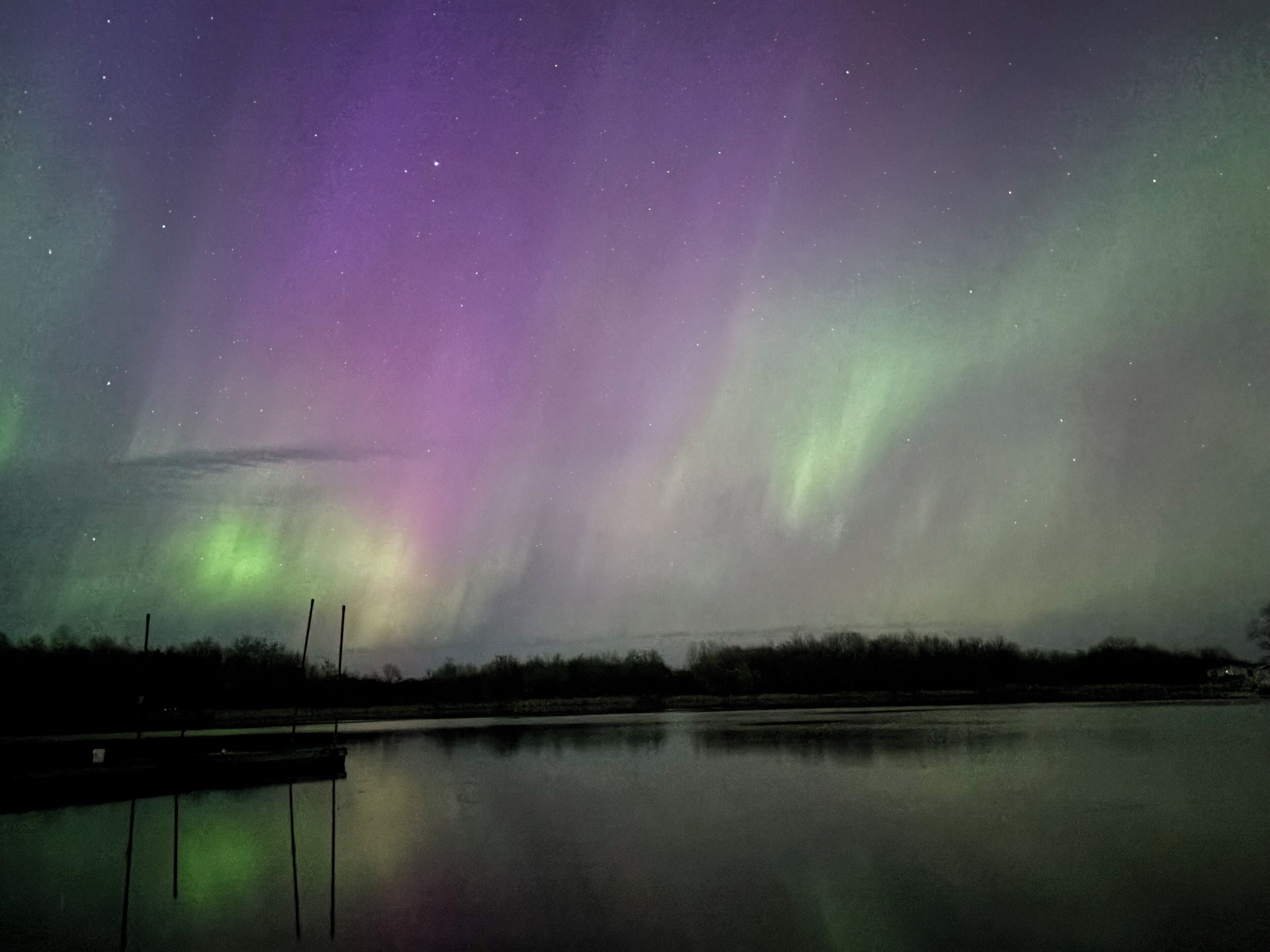 Ruhige Wasserfläche spiegelt den Nachthimmel mit sichtbaren Sternen und dem Polarlicht.