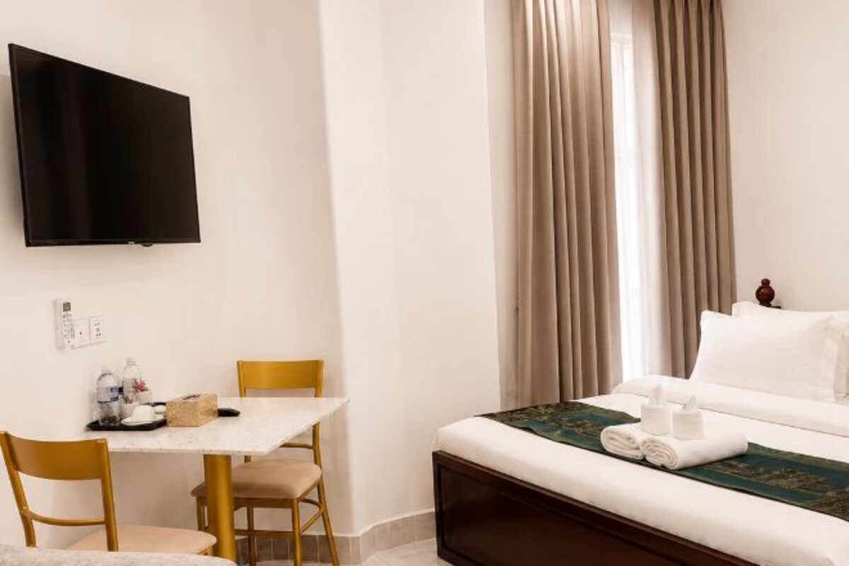 A hotel room with a bed, a TV mounted on the wall, a table with chairs, and a window with curtains.