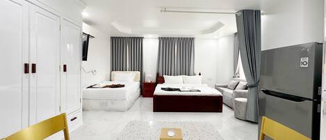 A modern hotel room with a large bed, a smaller bed, a sofa, a desk, and a wardrobe.