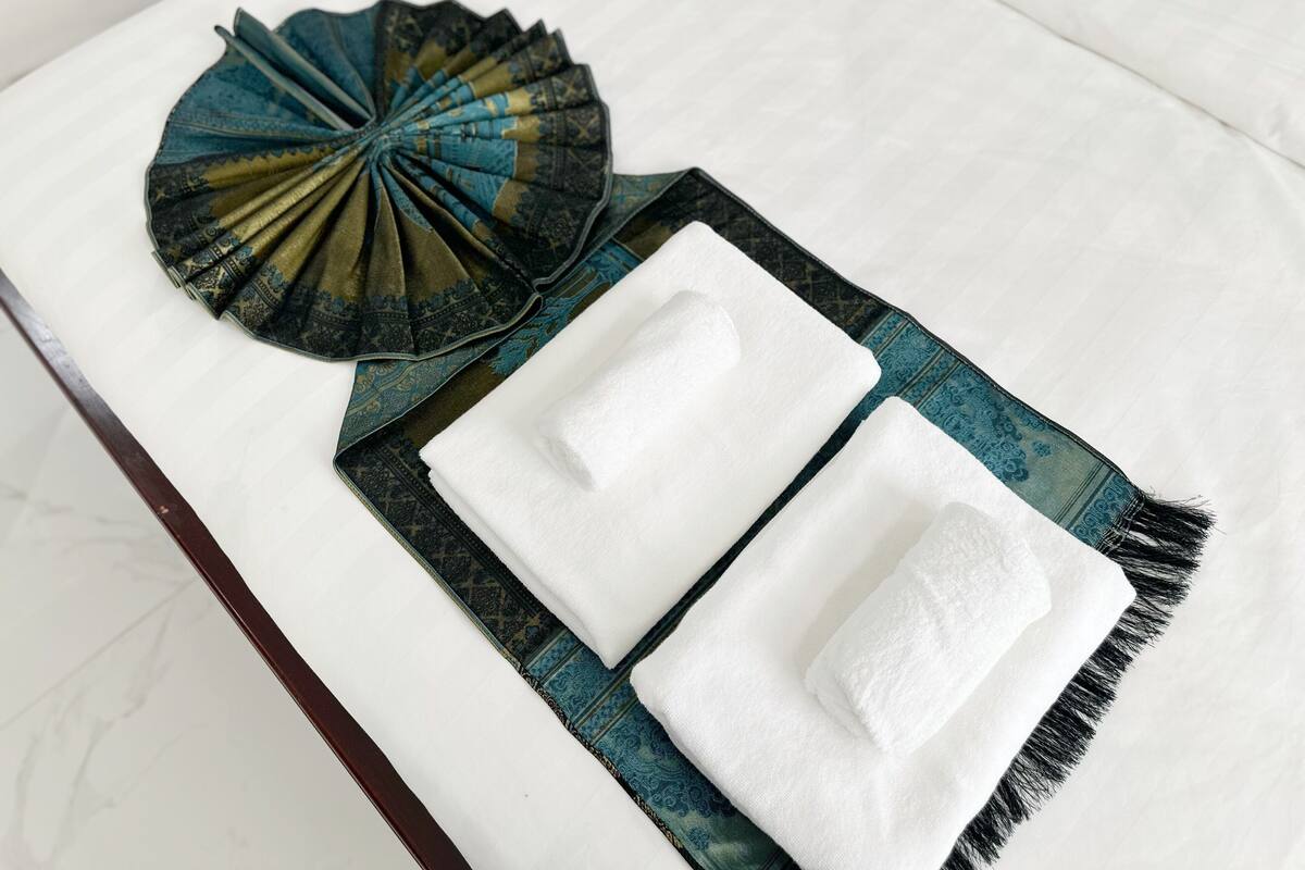 Een wit bed met twee witte handdoeken en een blauw geborduurd plaid.