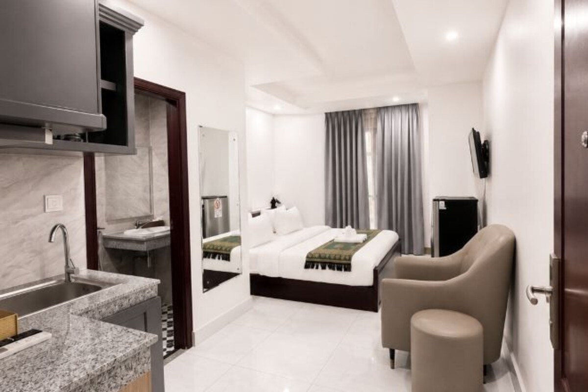 A modern hotel room with a bed, a seating area, a TV, and a kitchenette.