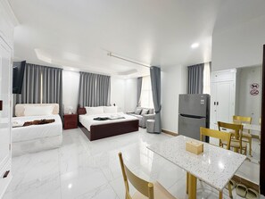 A modern hotel room with a bed, a sofa, a dining table, and a refrigerator.