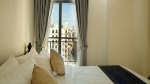 Ein Hotelzimmer mit Bett, Kissen, einem Fenster mit Vorhängen und Blick auf Gebäude.