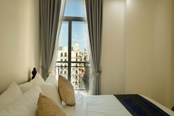 A hotel room with a bed, pillows, a window with curtains, and a view of buildings outside.