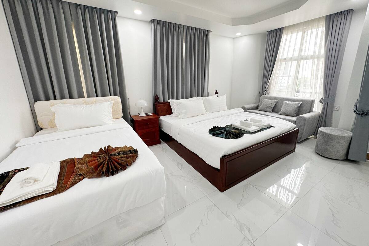 Een moderne hotelkamer met twee bedden, een slaapbank en een klein zithoekje.