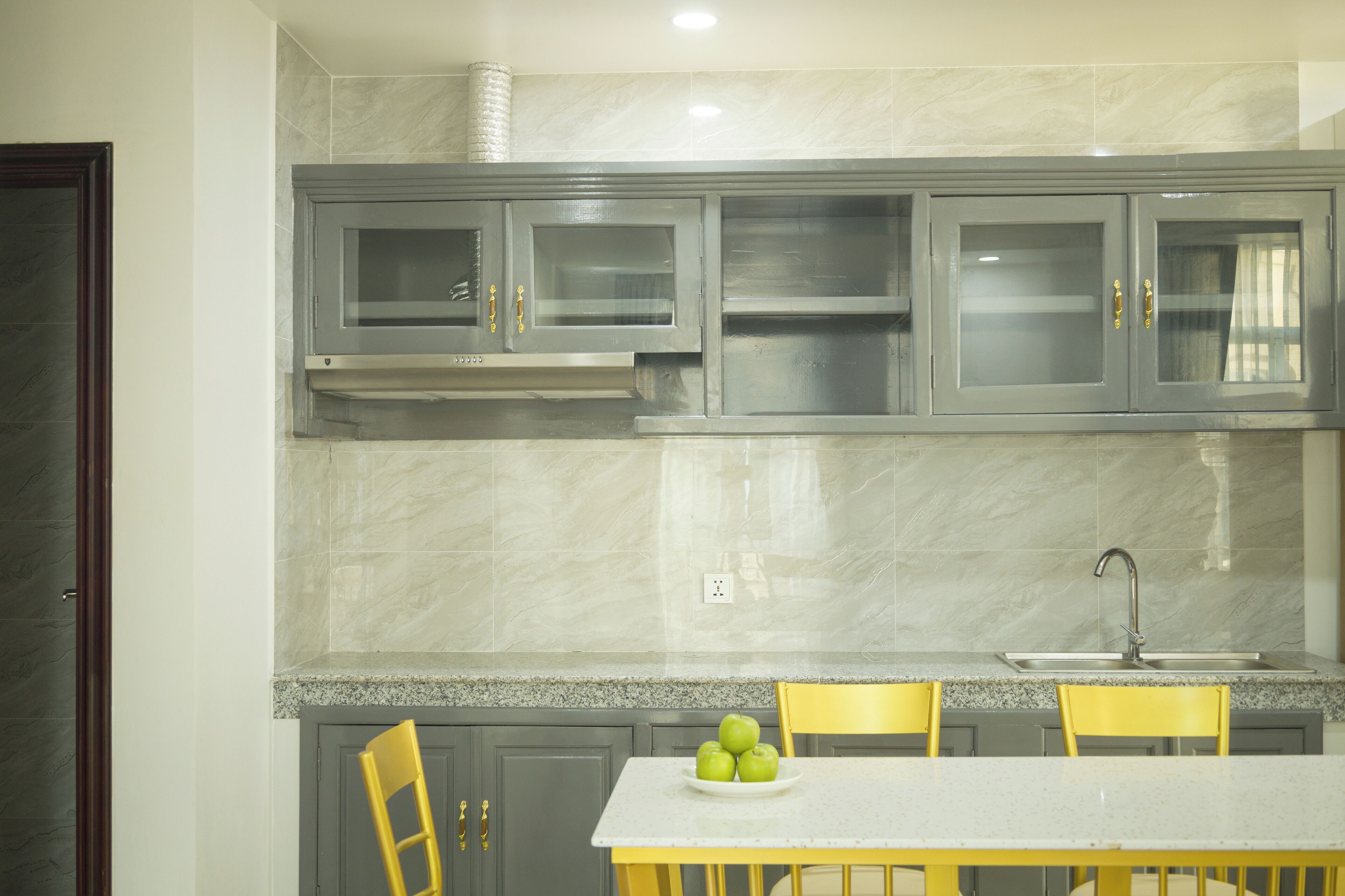 A kitchen with grey cabinets, a white countertop, and a yellow chair.