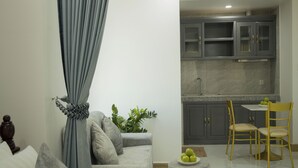 Ein modernes Wohnzimmer mit einem grauen Sofa, einem kleinen runden Hocker und einem Essbereich mit Tisch und Stühlen.