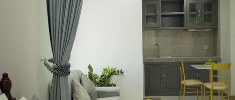 A modern living room with a grey sofa, a small round ottoman, and a dining area with a table and chairs.