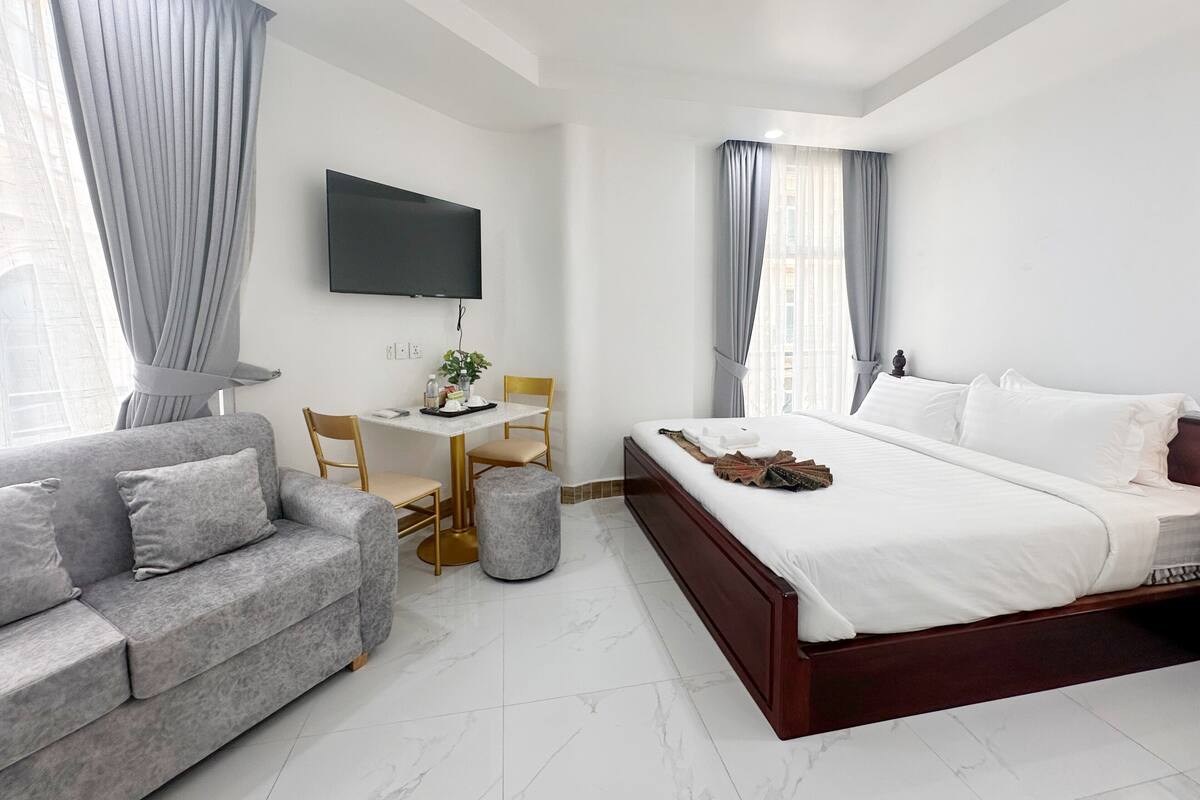 Een moderne hotelkamer met een groot bed, een bank, een kleine tafel met stoelen, een flatscreen televisie aan de wand en een raam met gordijnen.