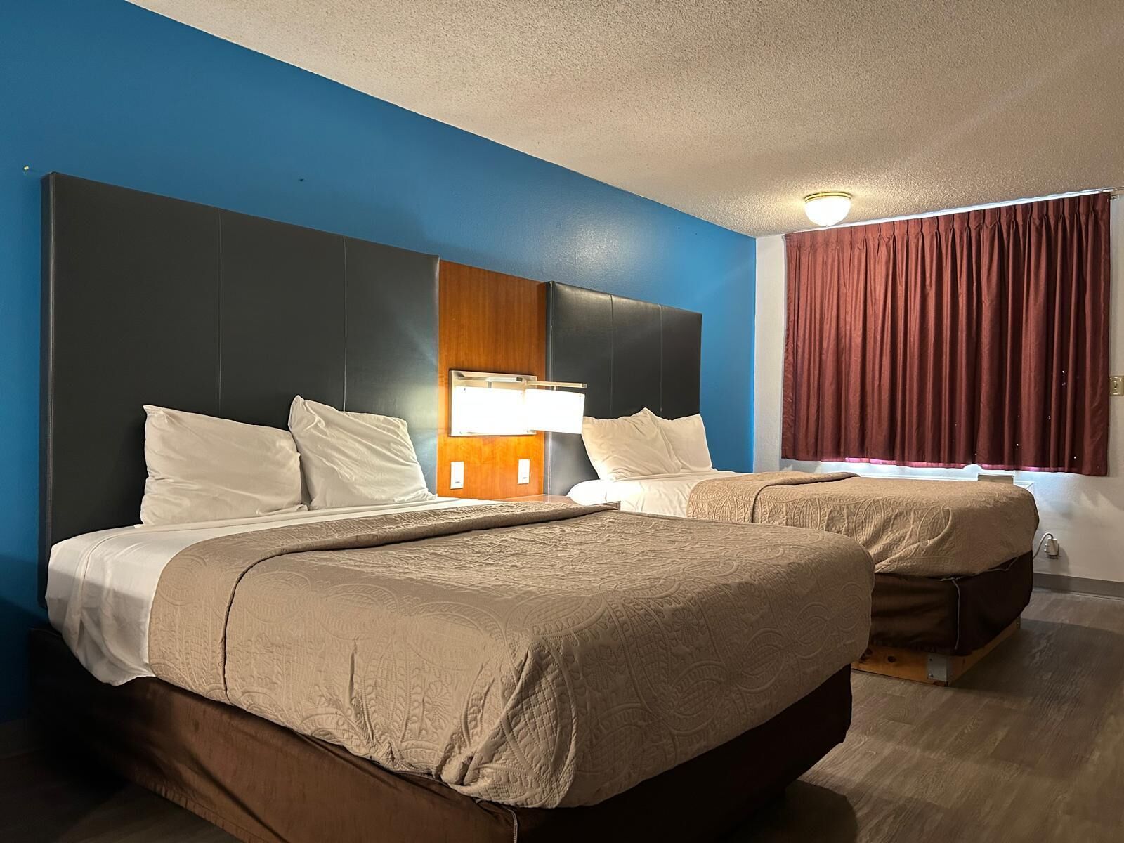 Ein Hotelzimmer mit zwei Betten, einem Holzkopfstück, einem Nachttisch, einer Lampe und einem Fenster mit Vorhängen.