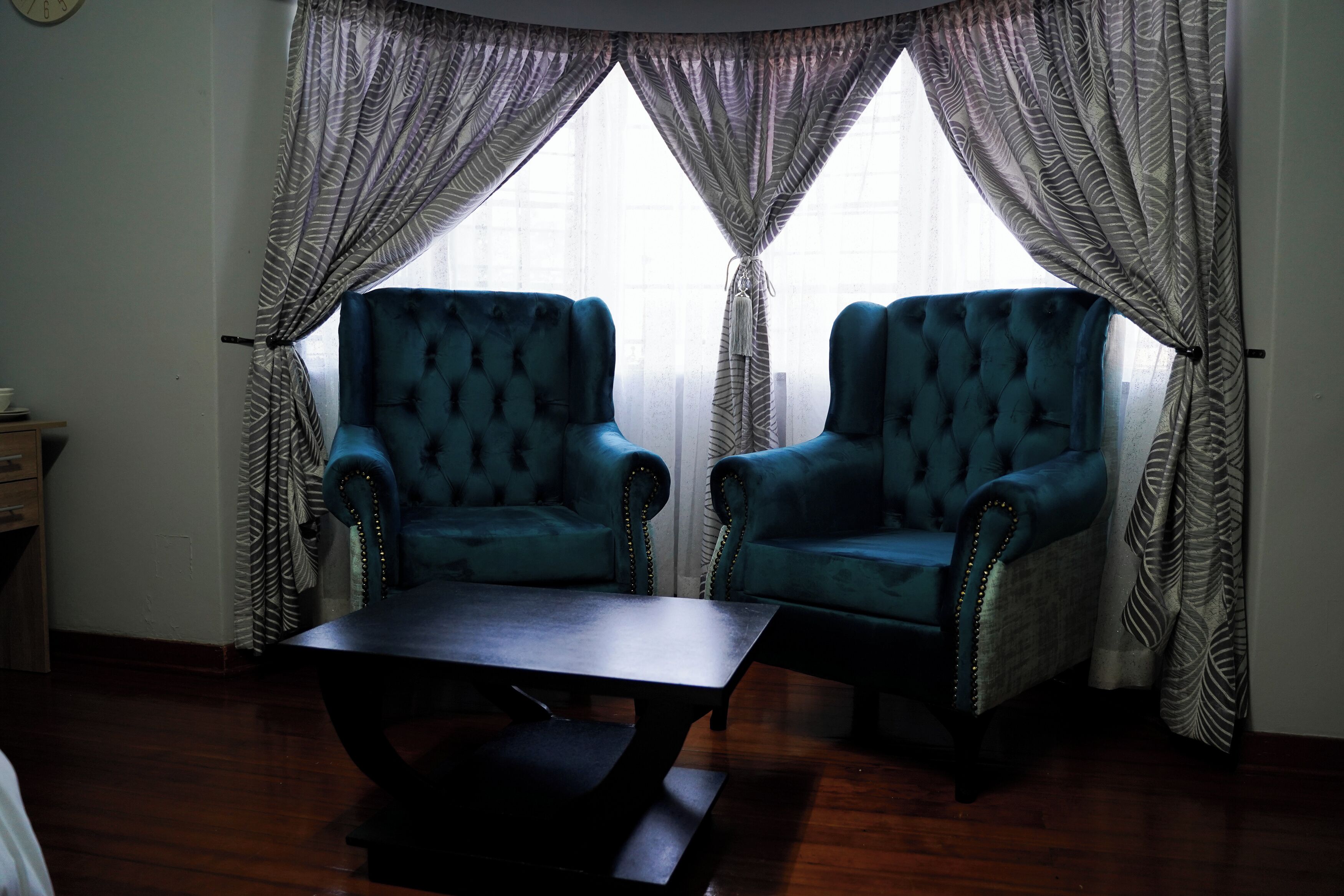 A room with two blue armchairs, a dark wooden coffee table, and patterned curtains.
