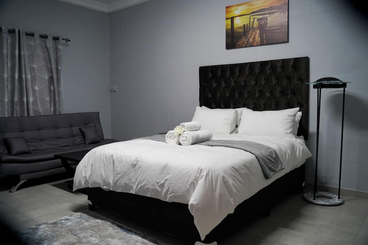 Ein modernes Schlafzimmer mit einem großen Bett, einem dunklen Kopfteil, einem grauen Sofa und einer Stehlampe.