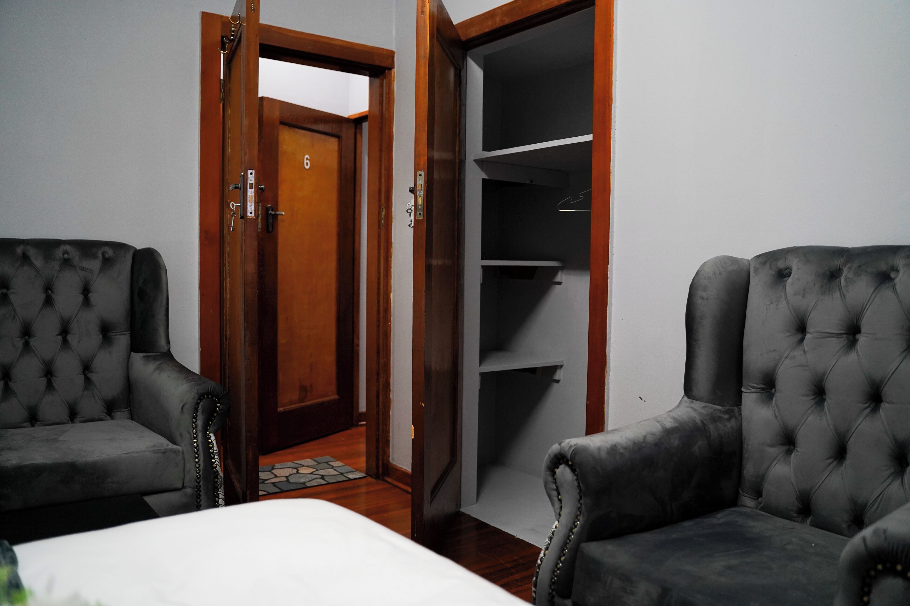 Una habitación con dos sillones tapizados, una puerta de madera con un número y un armario con estantes.