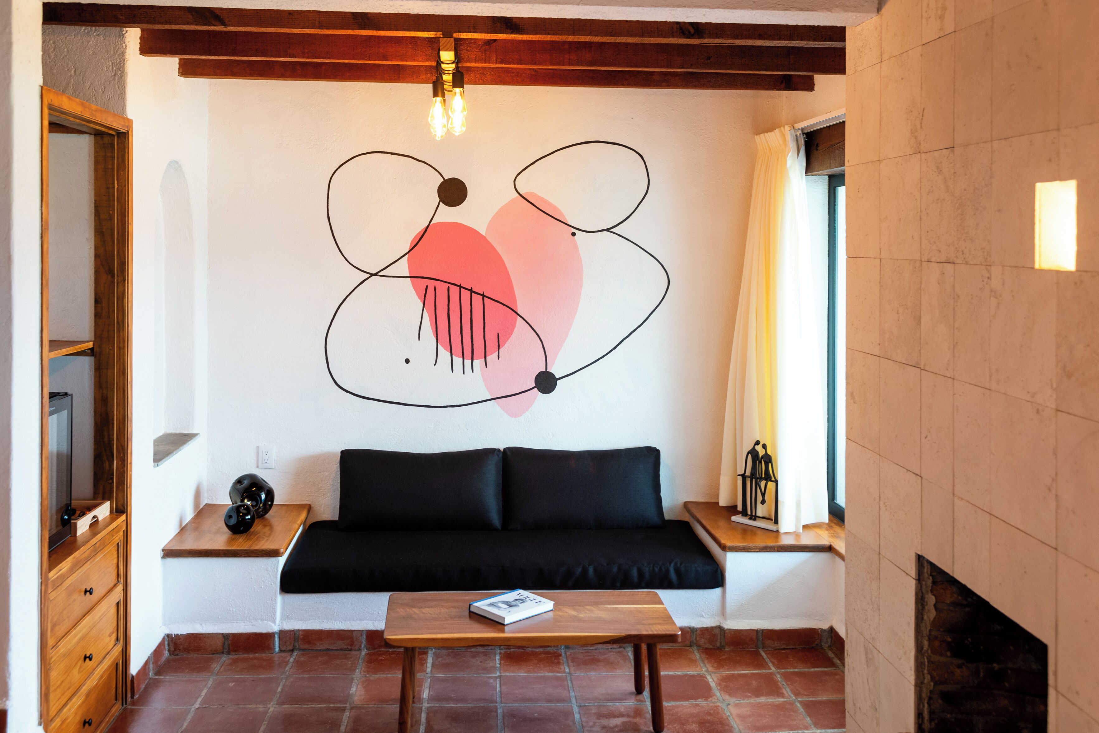 Un salon avec un canapé noir, une table basse en bois, un mur orné d’œuvres d’art abstraites, une cheminée et un meuble en bois.