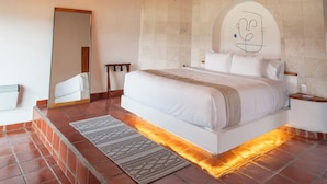 A bedroom with a large bed, a wooden ceiling, a tiled floor, and a wall-mounted light fixture.