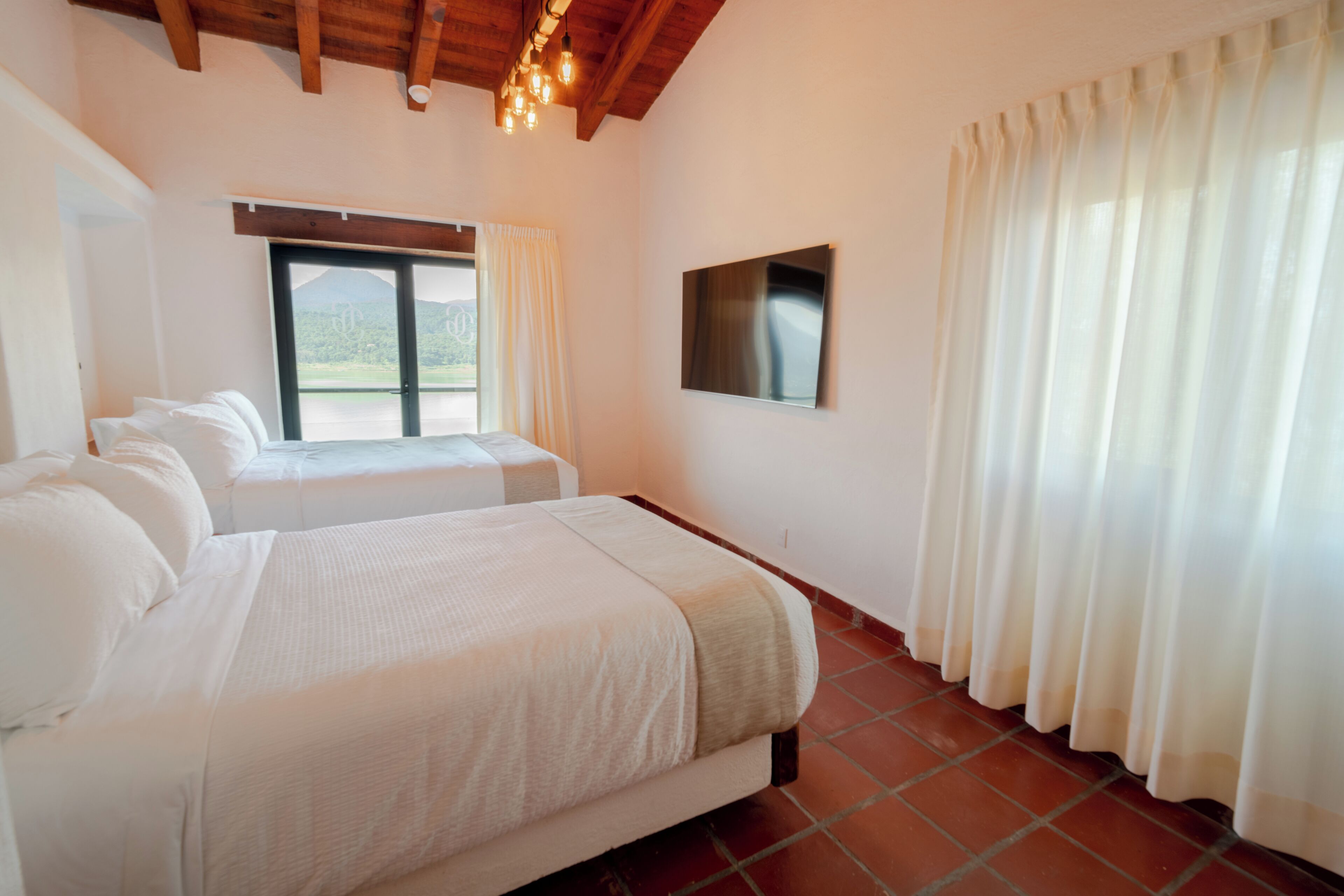 A bedroom with two beds, a TV, and a large window with curtains.