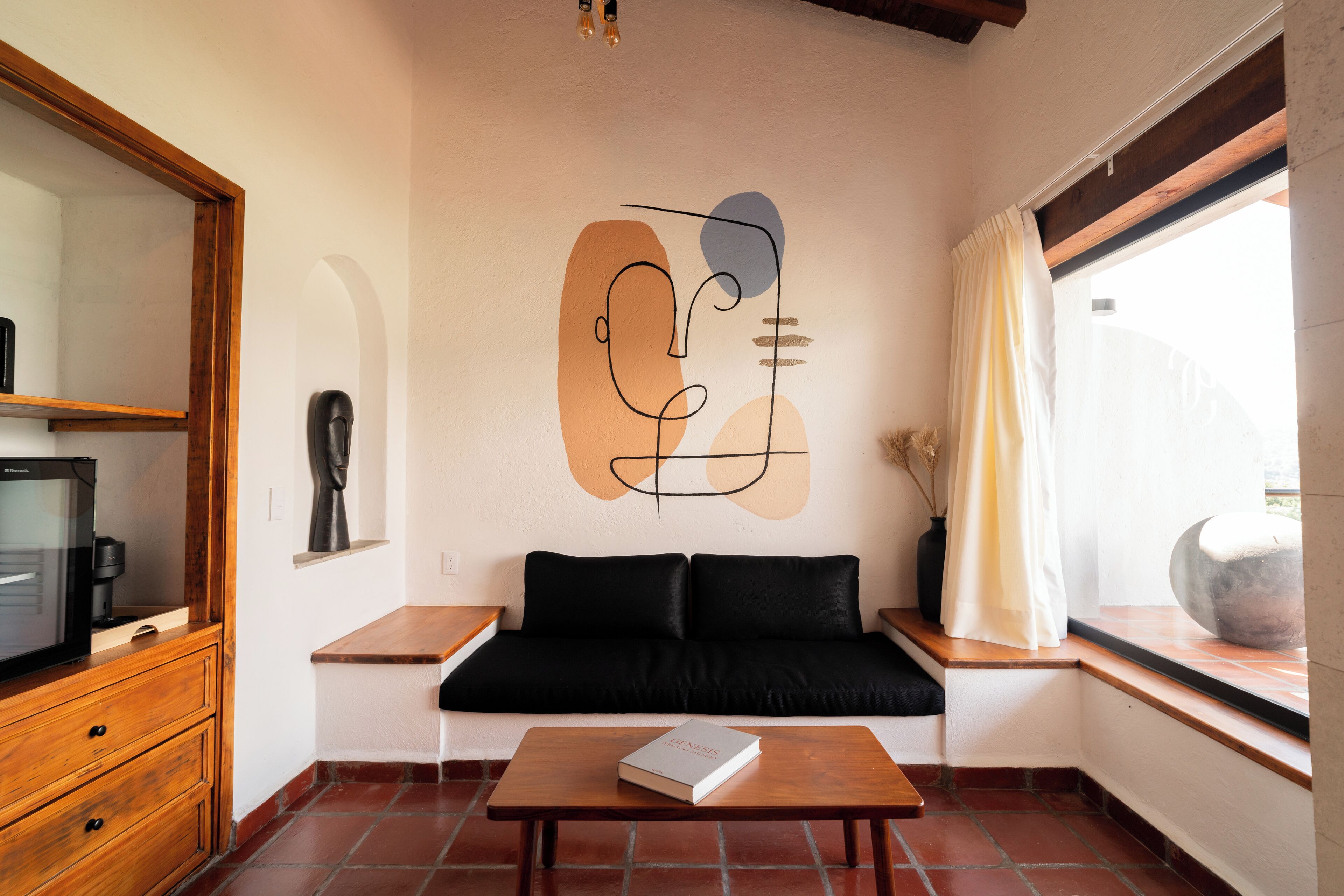 Una sala moderna con un sofá negro, una mesa de centro de madera y un mural en la pared.