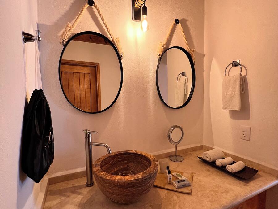 A bathroom with a wooden vanity, a round marble sink, two wall-mounted mirrors, a towel rack, and a small shelf with toiletries.