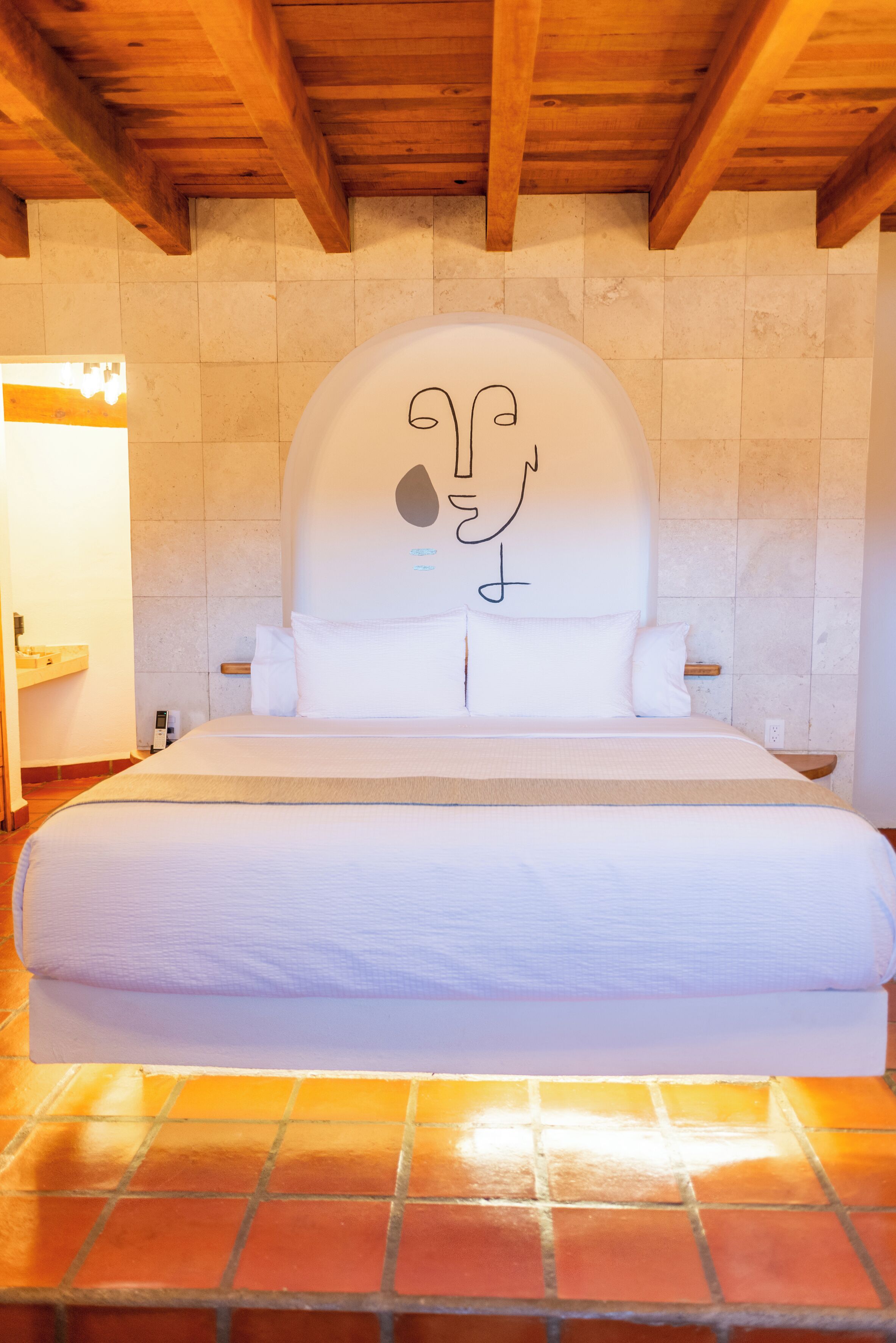 A bedroom with a large bed, a wooden ceiling, and a tiled floor.