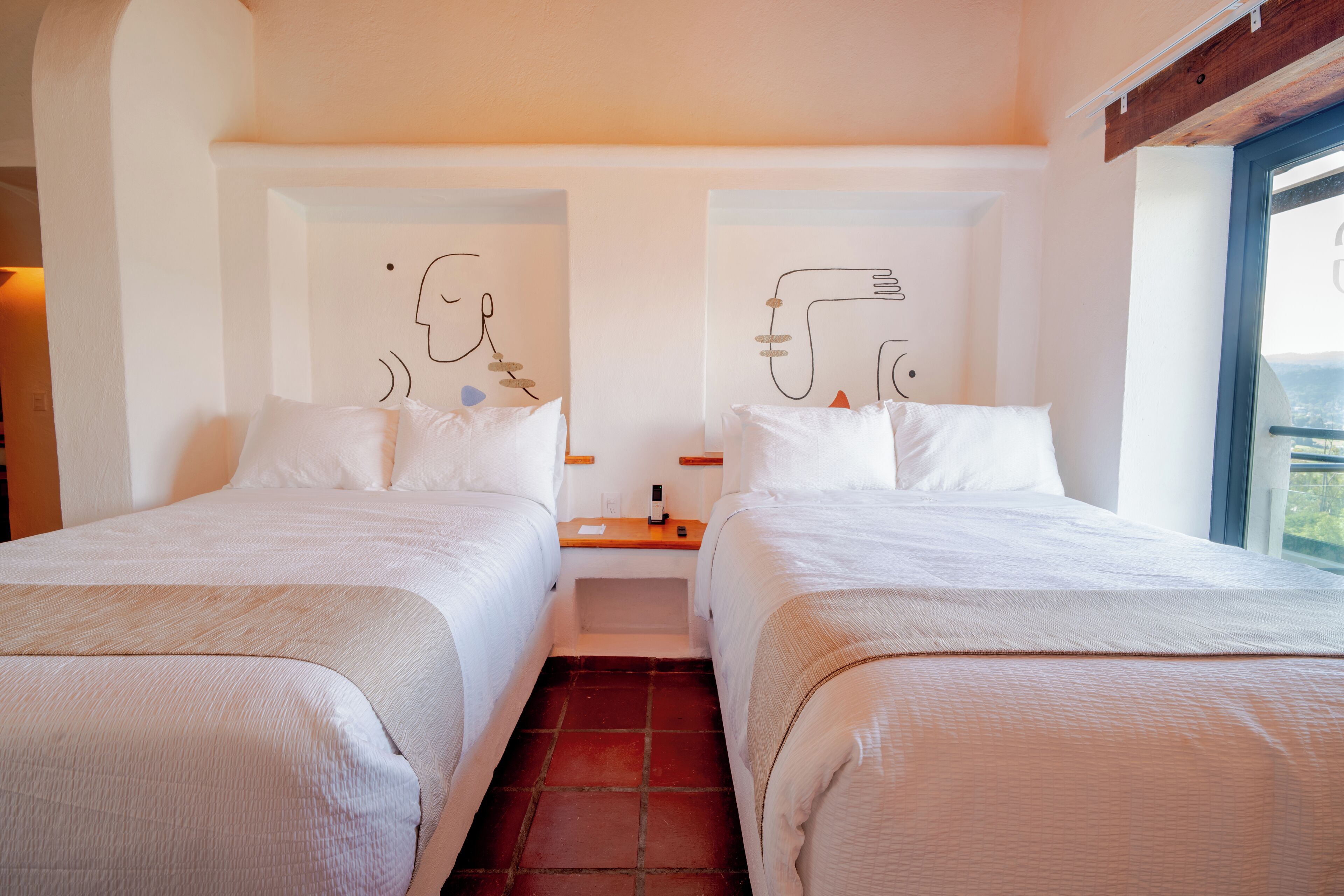 A hotel room with two beds, a nightstand, and artwork on the walls.