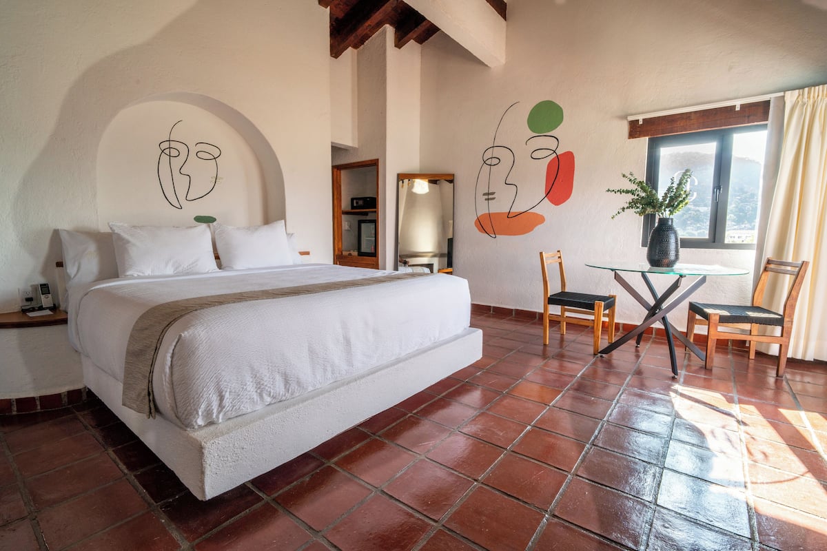 Una habitación de hotel con una cama grande, una mesita con sillas y una ventana con cortinas.
