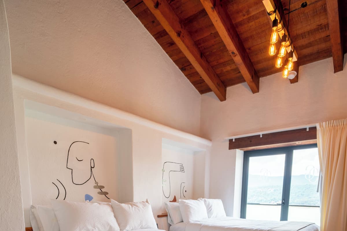 Un dormitorio con una cama grande, dos camas más pequeñas, techo de madera y una ventana con cortinas.