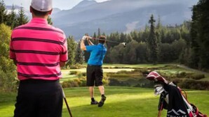 A golf course with a player in a blue shirt and a spectator in a pink striped shirt.