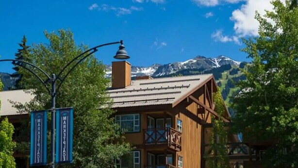 A wooden building with a balcony, surrounded by trees and mountains in the background.