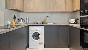 Een kleine keuken met houten kastjes, een ingebouwde wasmachine, een broodrooster en een spoelbak.
