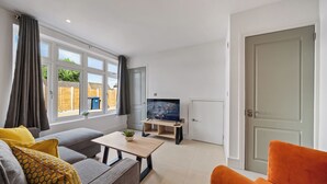 Een moderne woonkamer met een grijze bank, een oranje fauteuil, een houten salontafel en een tv op een dressoir.