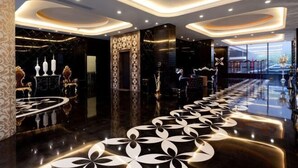 Un hall d’hôtel moderne avec un sol réfléchissant, un espace salon central et un plafond au motif original.
