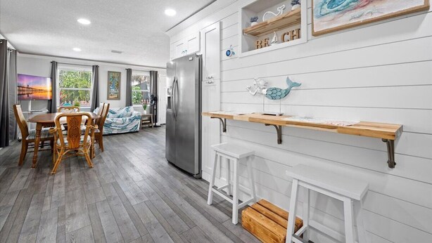 Een moderne keuken met witte kasten, een roestvrijstalen koelkast, een houten eettafel met stoelen en een klein witte kruk.