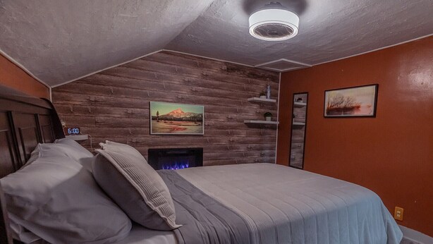 A bedroom with a wooden headboard, a bed with grey bedding, a fireplace, and a clock displaying 6:00. - Chic 1-bedroom apartment with WiFi, AC in fabulous Sheboygan (Sheboygan)