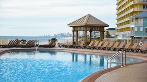 A pool area with lounge chairs and a gazebo, overlooking a city skyline and the ocean. - Treasure Island 2210 (Panama City Beach)