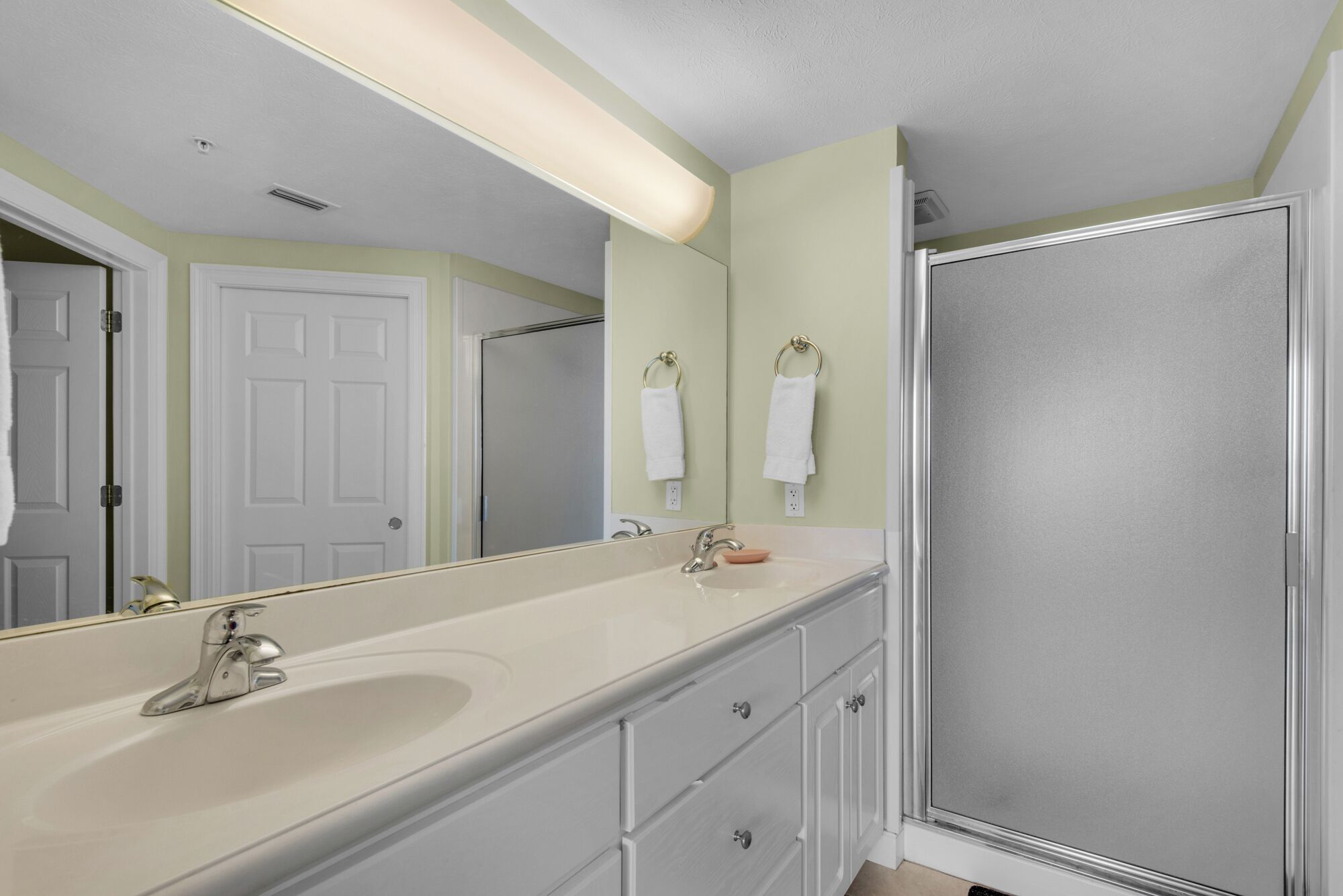 A bathroom with a large mirror, a sink, a shower, and a door.