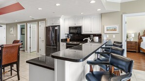 A modern kitchen with white cabinets, a black countertop, and a central island with bar stools. - Treasure Island 2210 (Panama City Beach)