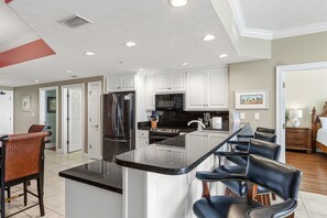 A modern kitchen with white cabinets, a black countertop, and a central island with bar stools. - Treasure Island 2210 (Panama City Beach)