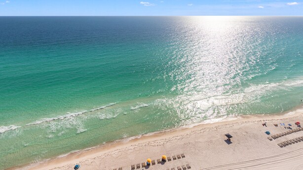 A beach with clear turquoise water, a sandy shore, and a few umbrellas and lounge chairs. - Treasure Island 2210 (Panama City Beach)