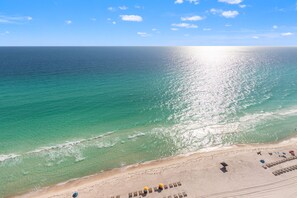 A beach with clear turquoise water, a sandy shore, and a few umbrellas and lounge chairs. - Treasure Island 2210 (Panama City Beach)