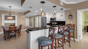Un'ampia cucina con isola centrale, sedie in legno, illuminazione a sospensione e frigorifero in acciaio inossidabile.