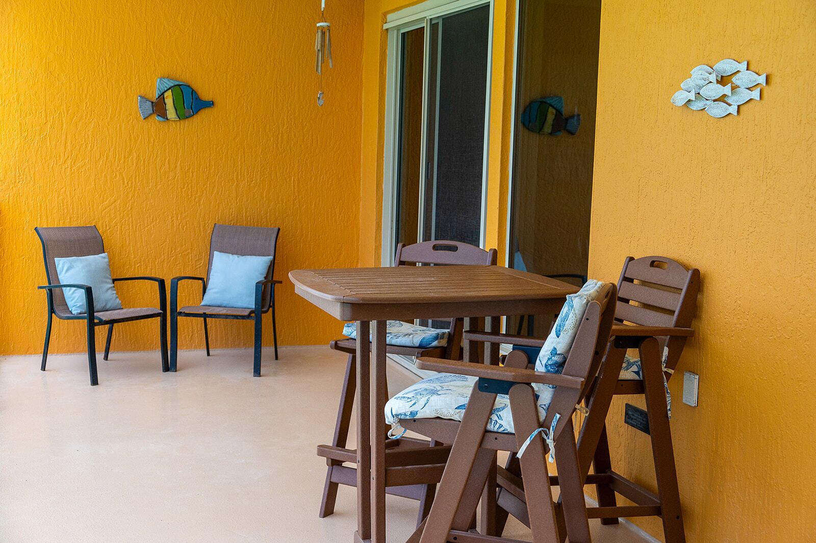 A room with a wooden table and four chairs, a sliding glass door, and decorative fish wall art.