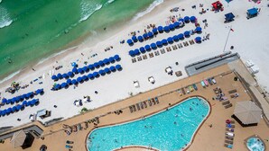 Vista aerea di un resort sulla spiaggia con una grande piscina, numerosi lettini e ombrelloni.