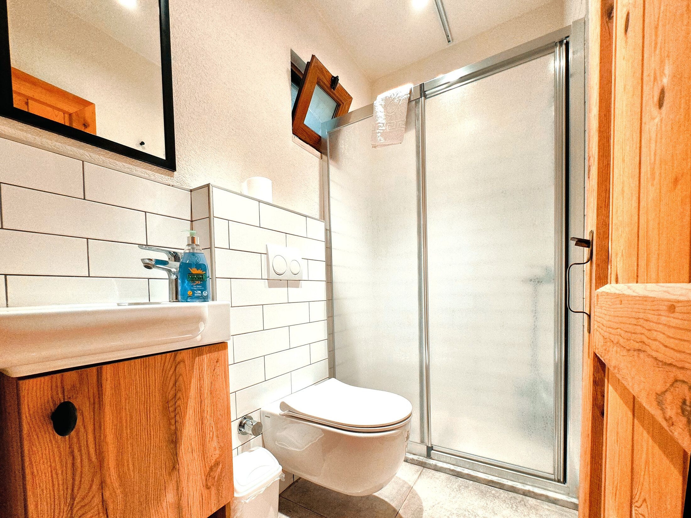 A bathroom with a white toilet, a sink with a wooden cabinet, a mirror, and a glass shower enclosure.