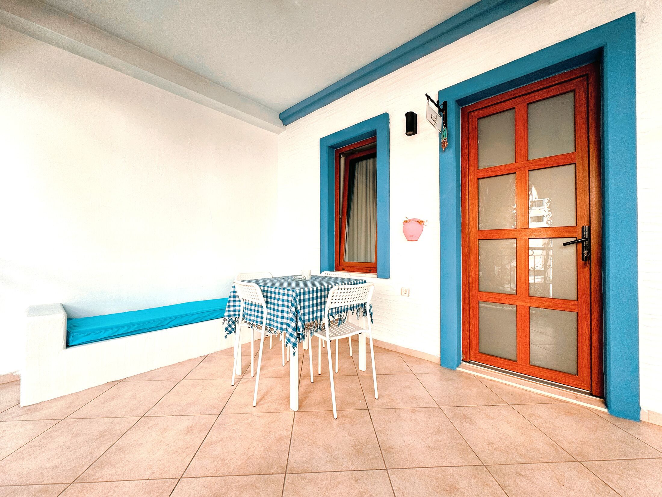Een klein terras met een tafel en stoelen, een deur met ruitpanelen en een blauw-witte muur.