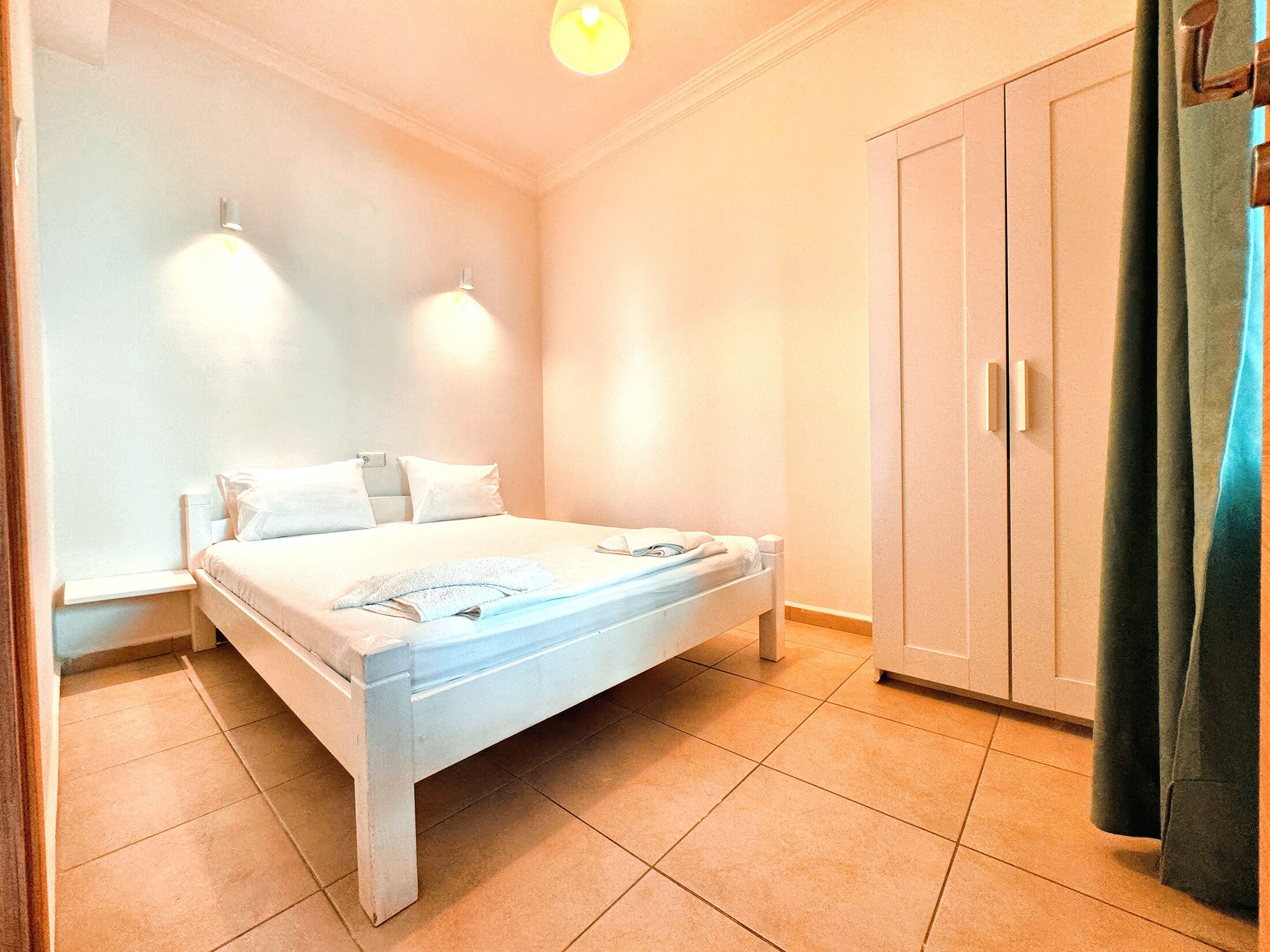 A bedroom with a bed, two wall-mounted lights, a wardrobe, and a window with curtains.