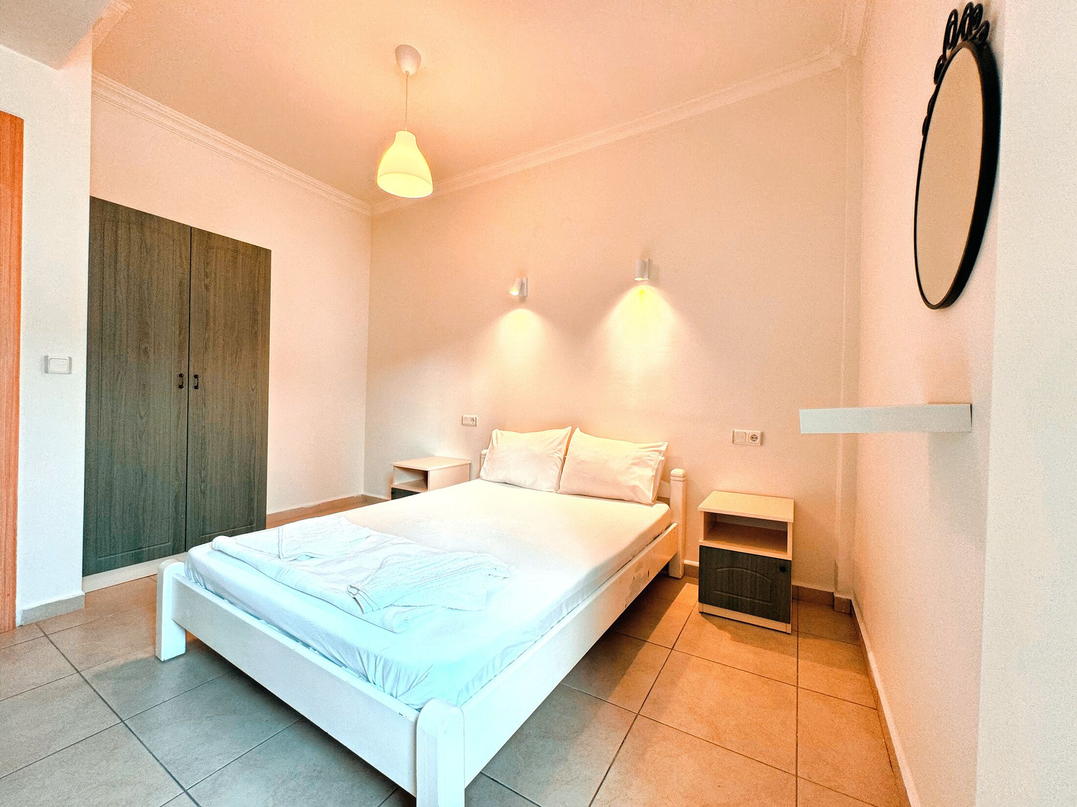 A bedroom with a large bed, bedside tables, a wardrobe, and a mirror on the wall.