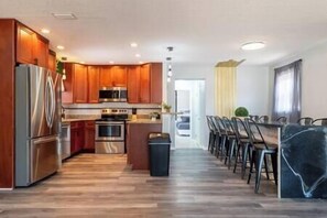 A modern kitchen with wooden cabinets, stainless steel appliances, and a central island with bar stools. - Cruise-Ready Oasis:15min to Beach & Port Canav w/ Huge Pool (Cocoa)